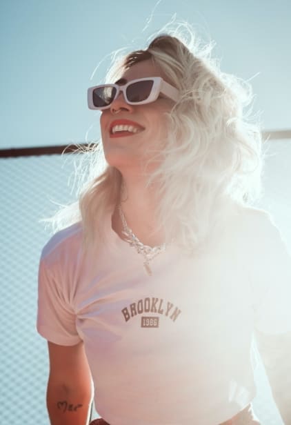 Woman in sunglasses and t-shirt smiling in the sun.
