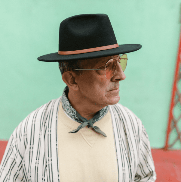 Older man in stylish glasses and hat posing in the street.